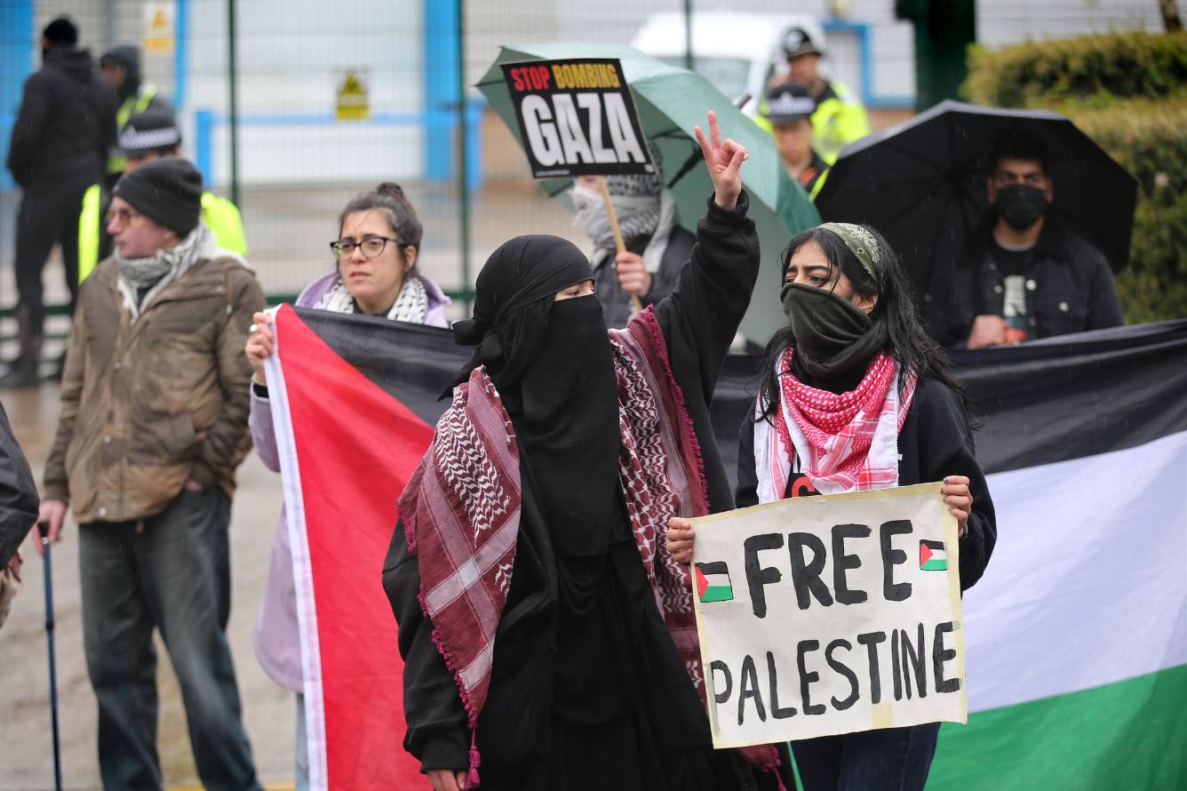 A protestor throws up a peace sign with her fingers while another holds a sign that says "Free Palestine".